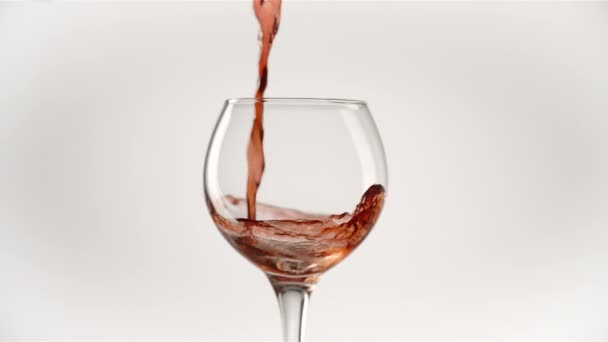 Αργή κίνηση του ρίχνει κόκκινο κρασί από το μπουκάλι στο κύπελλο σε λευκό φόντο — Αρχείο Βίντεο