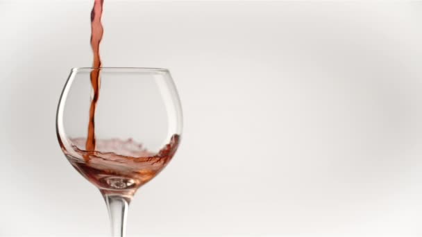 Rode wijn vormt een prachtige golf. Wijn gieten in wijnglas over witte achtergrond. Een close-up schot. Langzame beweging van het gieten van rode wijn uit fles in beker. — Stockvideo