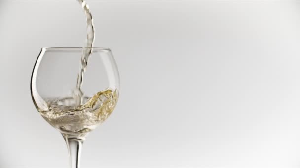 Beyaz şarap yuvarlak şarap bardağına dökülüyor. Düz beyaz bir zemin üzerinde. — Stok video