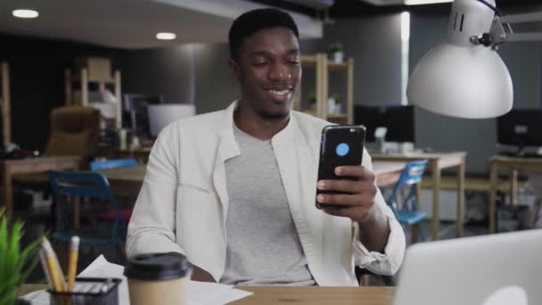 Portret młodego Afrykańczyka uśmiecha się i korzysta z telefonu w biurze — Wideo stockowe