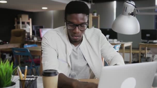 アフリカのビジネスマンはラップトップを使用しており、現代のオフィスで文書を見ています — ストック動画