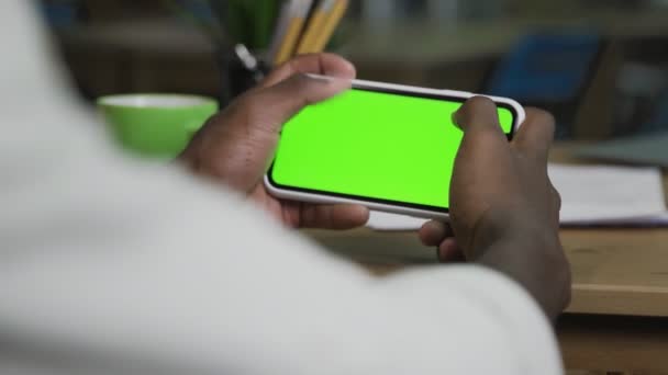 Hand of African American man scrolling web pages on horizontal Smartphone with green screen — Stock video