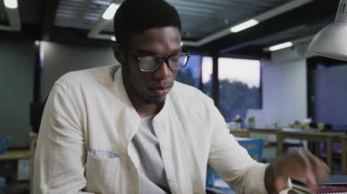 Gözlüklü genç Afrikalı ofis masasında oturuyor ve belgeleri okuyor.