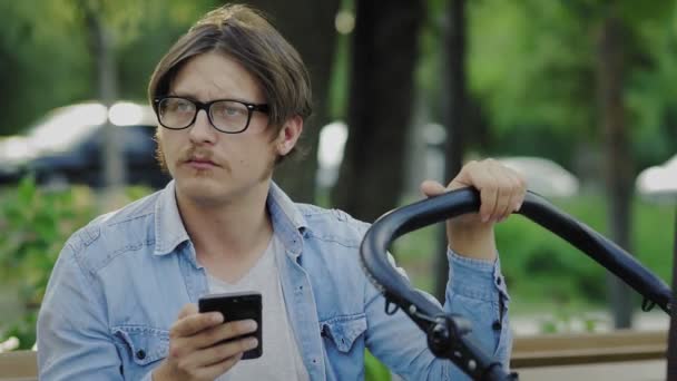 Father is using phone and swinging crying baby stroller. Father making a photo of baby — Stock Video