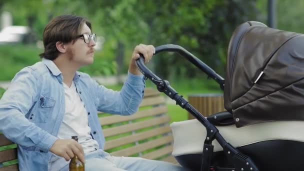 Zijaanzicht van aantrekkelijke man drinken van een biertje, terwijl swingende wandelwagen — Stockvideo