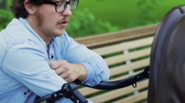 Genç baba bebek arabasını sallıyor ve bebeği süt şişesinden besliyor.