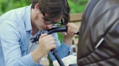 Yorgun baba dinlenirken uyuya kalıyor. Bebek parkında, sallanan bebek arabasıyla.