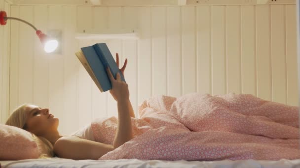 Mujer en ropa interior de noche terminó de leer libro, se apaga la luz y se va a dormir en la acogedora habitación del albergue — Vídeos de Stock