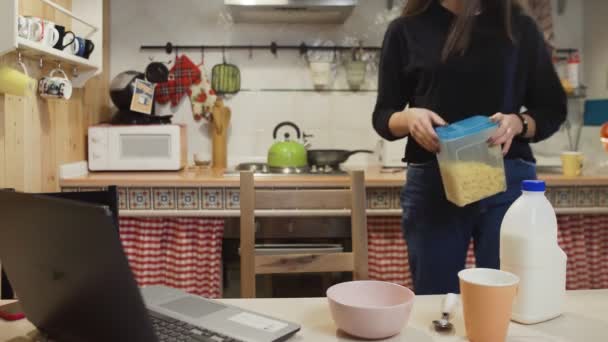 Giovane donna computer portatile di lavoro e mangia cereali fiocchi di mais a casa cucina. — Video Stock