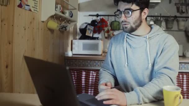 Jeune homme tenant sa carte de crédit sur le point de faire un achat en ligne sur ordinateur portable — Video