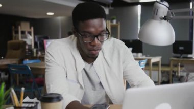 Portre genç Afrikalı Amerikalı adam dizüstü bilgisayarda çalışıyor ve ofiste telefon kullanıyor.