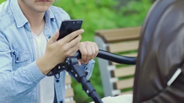 Großaufnahme: Vater benutzt Handy und schwingt weinenden Kinderwagen — Stockvideo