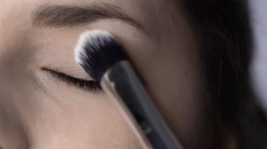 Stüdyoda oturan güzel ve muhteşem kadın için profesyonel makyaj süreci. Makyaj sanatçısı göz kapağına büyük bir fırça sürterek pudra sürüyor
