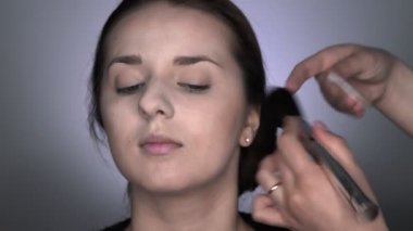 Stüdyoda oturan güzel ve muhteşem kadın için profesyonel makyaj süreci. Makyaj sanatçısı büyük bir fırçayla allık sürüyor