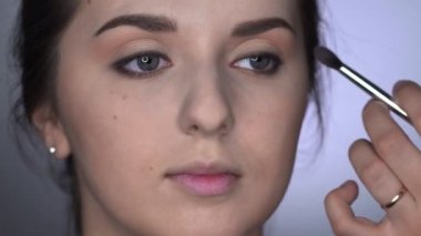Stüdyoda oturan güzel ve muhteşem kadın için profesyonel makyaj süreci. Makyaj sanatçısı göz kapağındaki fırçayla allık sürüyor