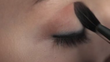 Güzellik stüdyosunda genç bir kadın için profesyonel makyaj yapıyor. Makyaj sanatçısı göz kapağındaki fırçayla allık sürüyor