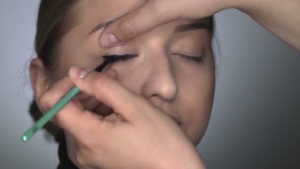 Makeup artist making professional make-up για νεαρή γυναίκα στο στούντιο ομορφιάς. Μακιγιάζ Καλλιτέχνης εφαρμόζει μαύρο eyeliner στο βλέφαρο — Αρχείο Βίντεο