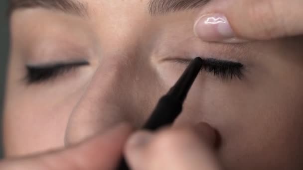 化妆艺术家在美容院为年轻女子做专业化妆。化妆师把黑色眼线笔涂在眼睑上 — 图库视频影像