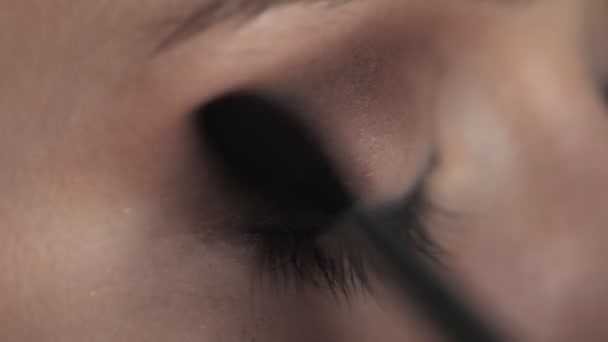 Makeup artist making professional make-up για νεαρή γυναίκα στο στούντιο ομορφιάς. Μακιγιάζ Καλλιτέχνης χρησιμοποιεί βούρτσα για να εφαρμόσει σκιά στο βλέφαρο — Αρχείο Βίντεο