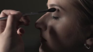 Makyaj sanatçısının güzellik salonunda genç bir bayana profesyonel makyaj yapması. Makyaj sanatçısı göz kapağına gölge uygulamak için fırça kullanır