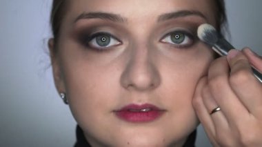 Güzellik stüdyosunda genç bir kadın için profesyonel makyaj yapan makyözlere yakın çekim. Makyaj sanatçısı göz kapağına gölge uygulamak için fırça kullanır