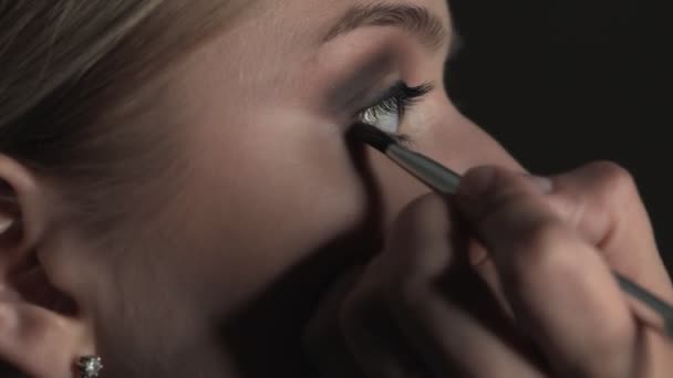 Sidovy av makeup artist gör professionell make-up för ung kvinna i skönhetsstudio. Make up Artist använder borste för att applicera skugga på ögonlocket — Stockvideo