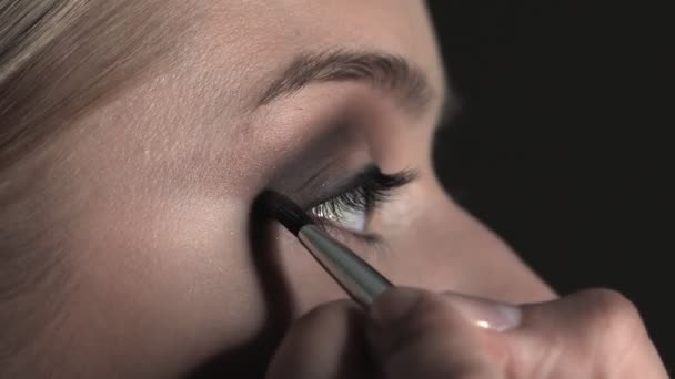 Vue latérale du maquilleur faisant du maquillage professionnel pour jeune femme dans un studio de beauté. Make up Artist utilise le pinceau pour appliquer une ombre sur la paupière — Video