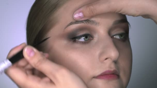 Nahaufnahme einer Visagistin, die junge Frauen im Schönheitsstudio professionell schminkt. Make-up Artist zeichnet Pfeile über Auge, Eyeliner — Stockvideo
