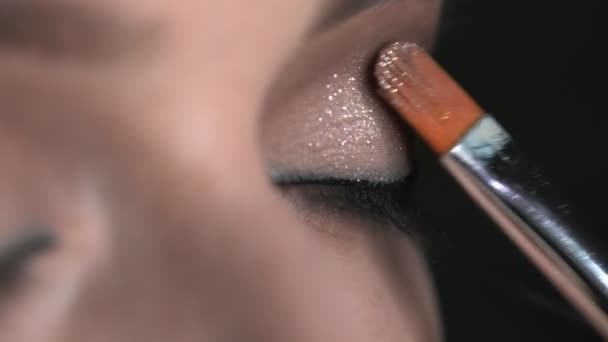 Macro de Maquillaje artista haciendo maquillaje profesional para mujer joven en el estudio de belleza. Maquillaje Artista utiliza cepillo para aplicar brillo en los ojos — Vídeo de stock