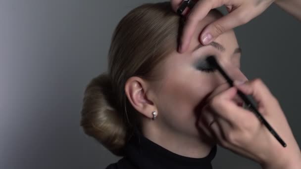 Maquillaje artista haciendo maquillaje profesional para mujer joven en el estudio de belleza. Maquillaje Artista hace que el maquillaje ojos ahumados de un tono negro con cepillo especial de un hermoso modelo — Vídeos de Stock