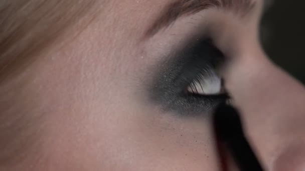 Boční pohled make-up umělce dělat profesionální make-up pro mladou ženu v beauty studiu. Make-up umělec dělá make-up kouřové oči černého odstínu se speciálním štětcem krásného modelu — Stock video