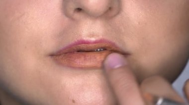Güzellik stüdyosunda genç bir kadın için profesyonel makyaj yapıyor. Makyaj sanatçısı model üzerine ruj sürüyor