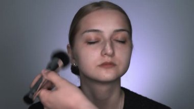 Güzellik stüdyosunda genç bir kadın için profesyonel makyaj yapıyor. Makyaj sanatçısı tozu büyük bir fırçayla uygular