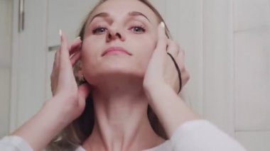 Genç bir kadın saçını elastik bir bandın içine sokuyor ve kameraya bakıyor.