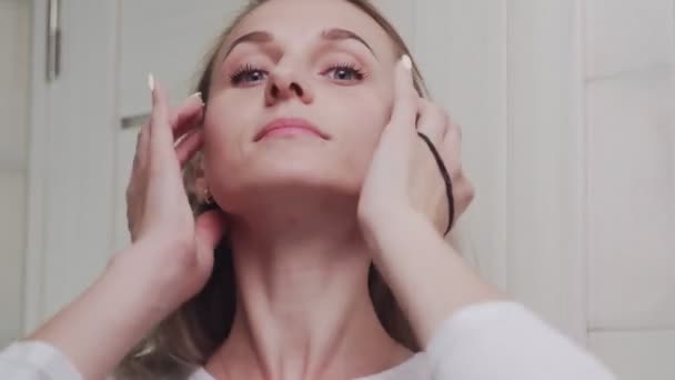 Uma jovem mulher coloca o cabelo em uma faixa elástica e olha para a câmera — Vídeo de Stock