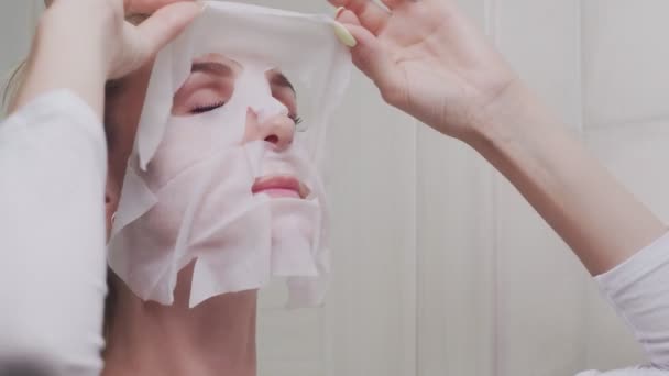 Клоуз женщины снимает маску на лице, глядя в зеркало — стоковое видео