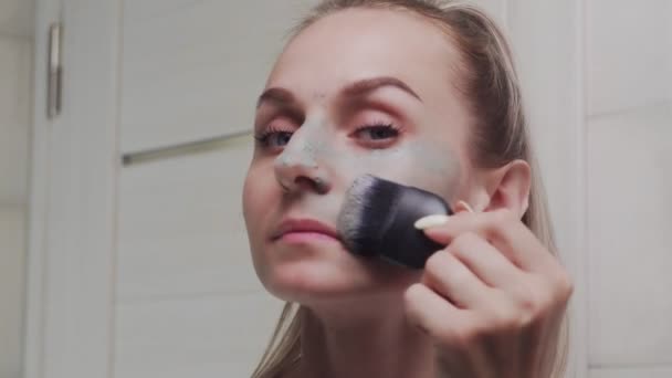 Close-up van de vrouw toepassen van klei masker op haar gezicht kijken naar de camera — Stockvideo