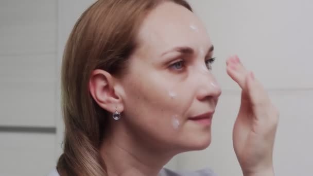 Donna adulta che applica la crema e guardando allo specchio godere di bellezza naturale e sano — Video Stock