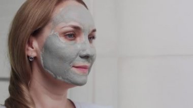 Yetişkin bir kadının kameraya bakarak yüzüne kilden maske takması.