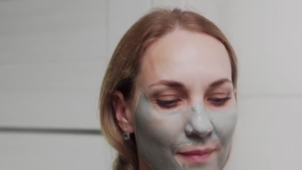 Primer plano de la mujer adulta aplicando máscara de arcilla en su cara mirando a la cámara — Vídeo de stock