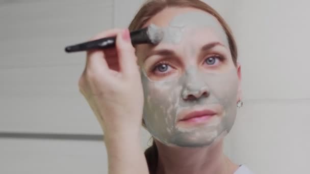 Close up of Adult woman applying clay mask on her face looking at the camera — Stock Video