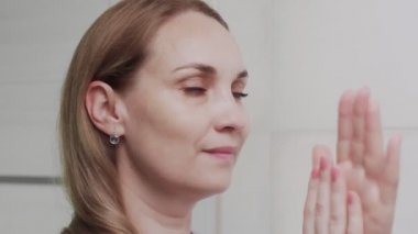 Yetişkin bir kadın losyon veya yağ sürüyor ve aynaya bakıyor.