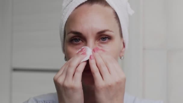 Mujer adulta con una toalla en la cabeza aplicando crema y mirando a la cámara — Vídeo de stock