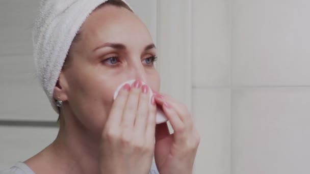 Volwassen vrouw met een handdoek op haar hoofd aanbrengen lotion en kijken in spiegel genieten van natuurlijke schoonheid en gezond — Stockvideo