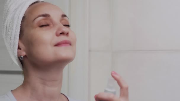 Закрыть взрослую женщину с полотенцем на голове, нанося водяной спрей для увлажнения кожи — стоковое видео