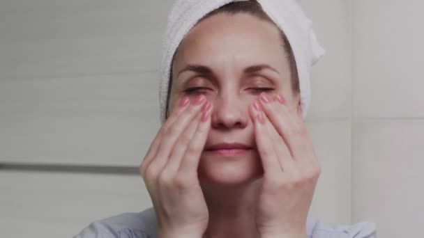 Женщина с полотенцем на голове наносит лосьон или масло и смотрит в камеру — стоковое видео