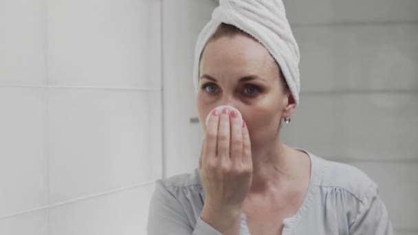 Volwassen vrouw met een handdoek op haar hoofd aanbrengen lotion en kijken in spiegel genieten van natuurlijke schoonheid en gezond — Stockvideo