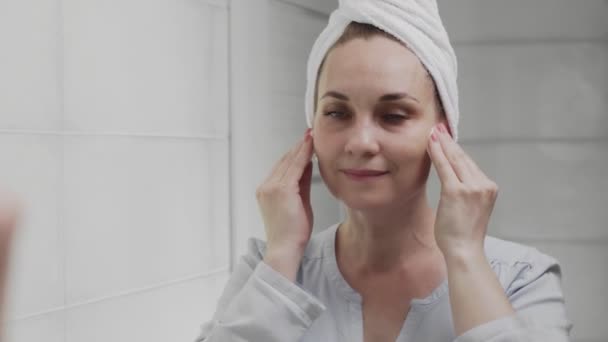 Dorosła kobieta z ręcznikiem na głowie stosując balsam i patrząc w lustro cieszyć się naturalne piękno i zdrowe — Wideo stockowe