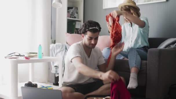 Mädchen mit Hut auf der Couch und ein Mann mit Laptop, der unterwegs Dinge sortiert — Stockvideo