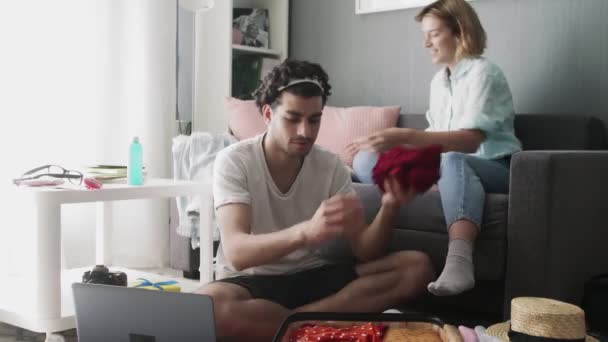 Mladý pár vybalit oblečení z kufru a mluvit spolu — Stock video